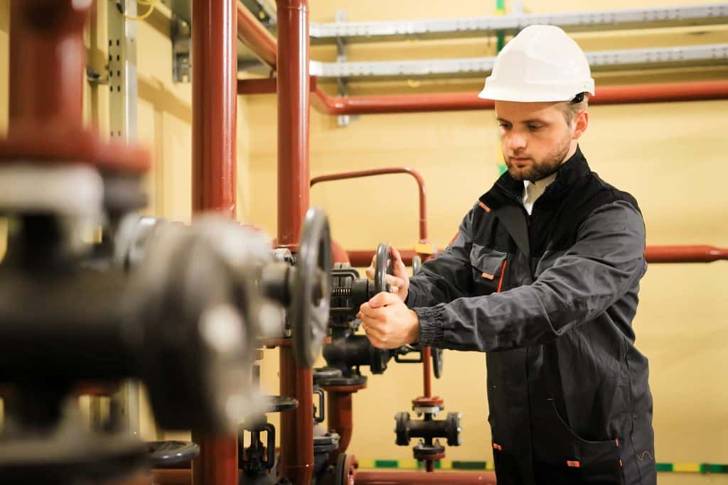worker with protective helmet turns valve on industrial refinery oil pipes
